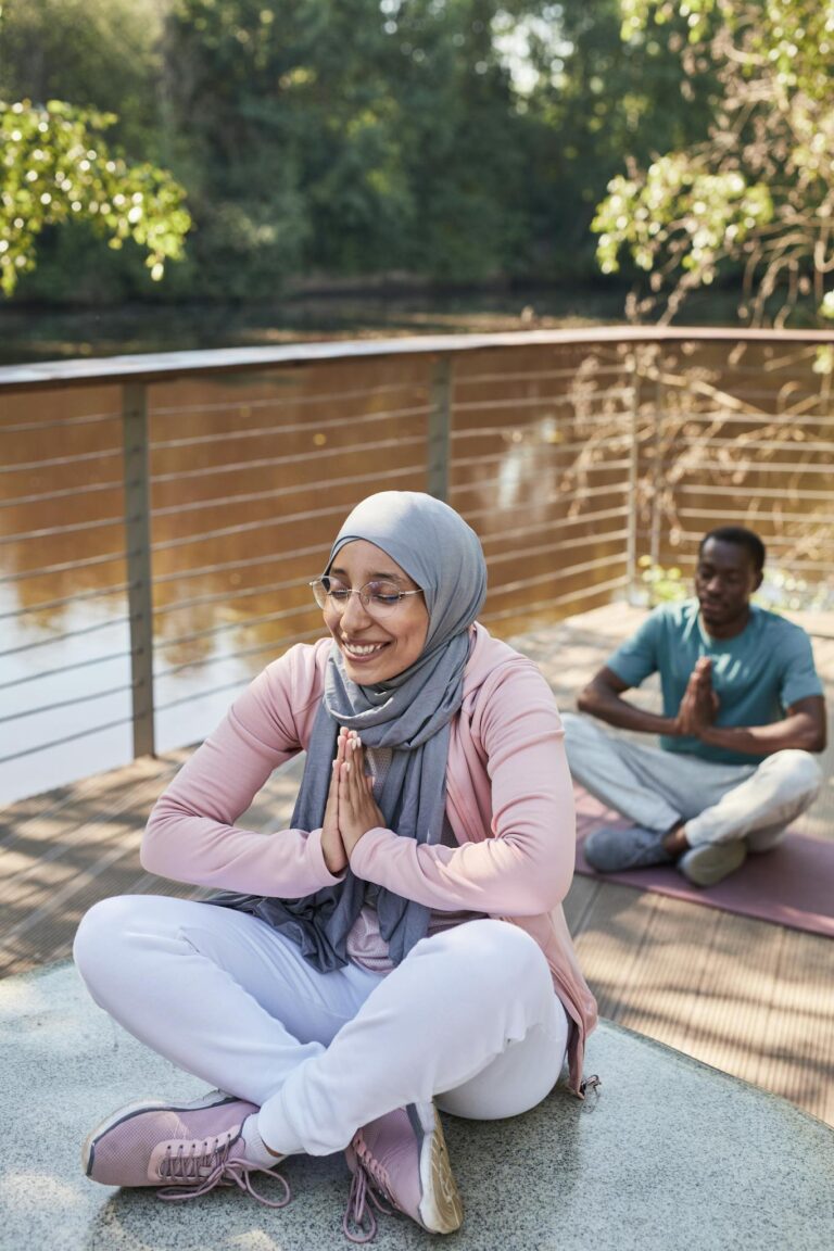 A diverse group meditating outdoors by the river, embracing wellness.